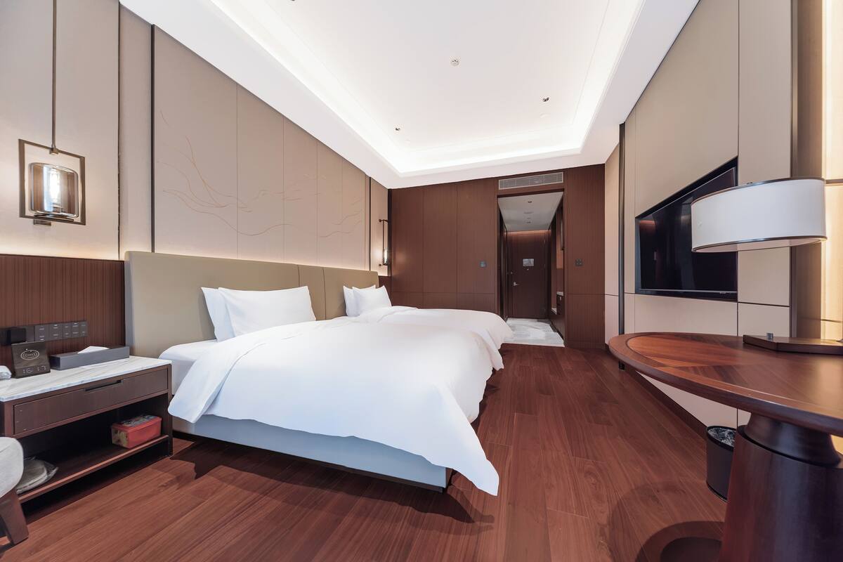 A modern hotel room with a large bed, bedside tables, a desk, and a TV.