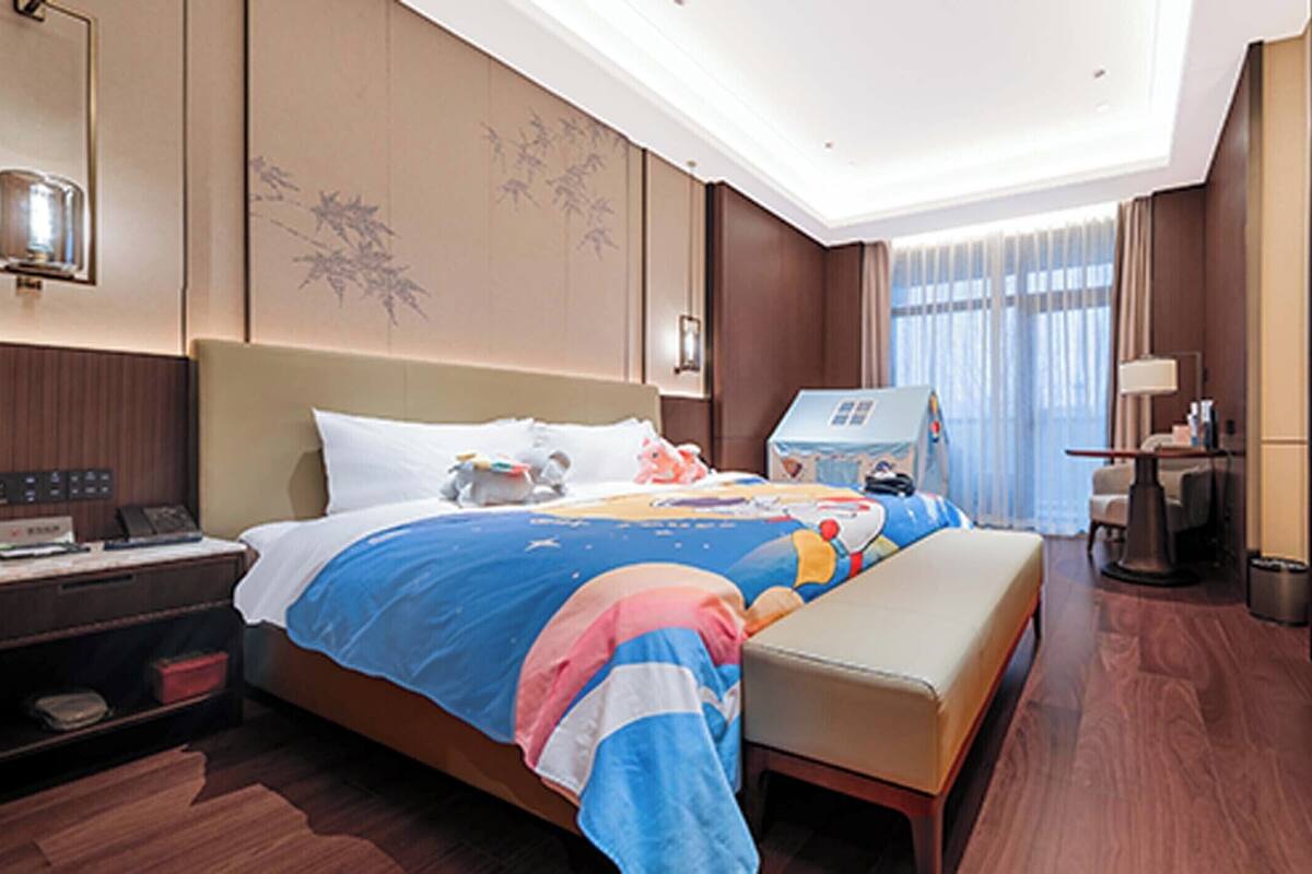 A modern hotel room with a large bed, bedside tables, a desk, and a TV.