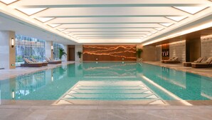 Una piscina interior con agua cristalina, sillas de descanso y un diseño de techo moderno.