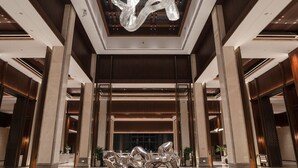 Un hall amplio con una gran escultura abstracta de metal, una fuente y un suelo estampado.