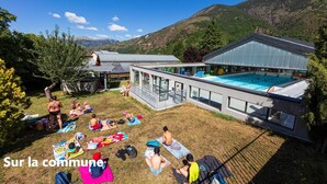 Zona de piscina con gente tomando el sol y nadando, rodeada de montañas.