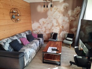 Un salon moderne avec un mur en bois, un canapé agrémenté de coussins à motifs, une table basse sur laquelle sont posés des papiers et un tapis de course.