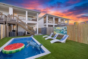 A two-story house with a swimming pool, a wooden deck, and a mural on the fence.