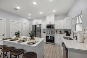 A modern kitchen with white cabinets, stainless steel appliances, and a central island with bar stools. - Private Pool • Xbox Gaming Wall • King Suites • Sleeps 14 • Beach Unit A (Panama City Beach)
