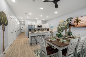 A modern kitchen with white cabinets, a central island, and a dining area with a wooden table and white chairs.