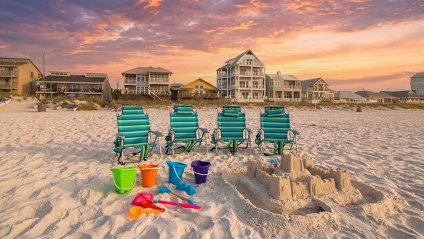 A beach with beach chairs, buckets, and a sandcastle.