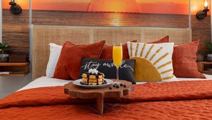 A bed with a sunset view, a plate of pancakes, and a 'stay awhile' pillow.