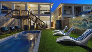 A two-story house with a swimming pool, outdoor seating, and a mural.