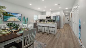 A modern kitchen with white cabinets, a central island, bar stools, and a ceiling fan.