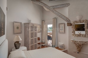A bedroom with a bed, a nightstand, a lamp, a wardrobe, a mirror, and a view of the outdoors.