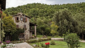 A stone building with a balcony, surrounded by a well-maintained garden and a forested hillside. - Borgo La Ferriera (Celleno)