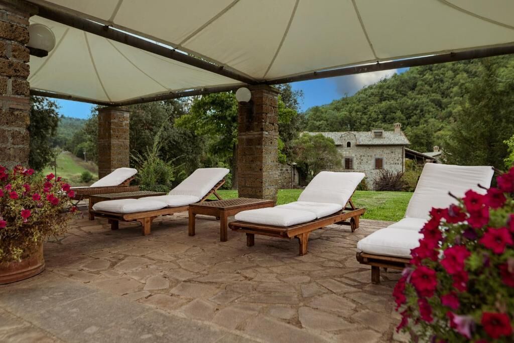 A covered outdoor seating area with stone flooring and wooden lounge chairs.