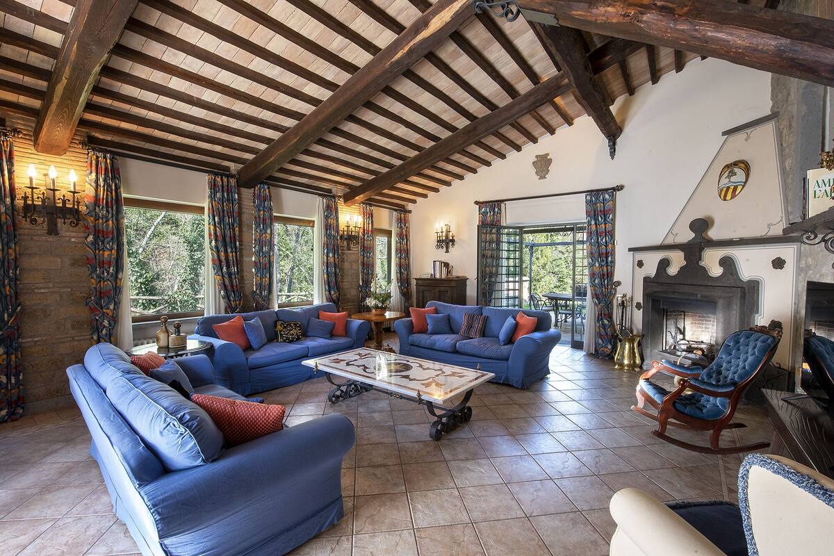 A spacious living room with a high wooden ceiling, a fireplace, and a large window providing a view of the outdoors.