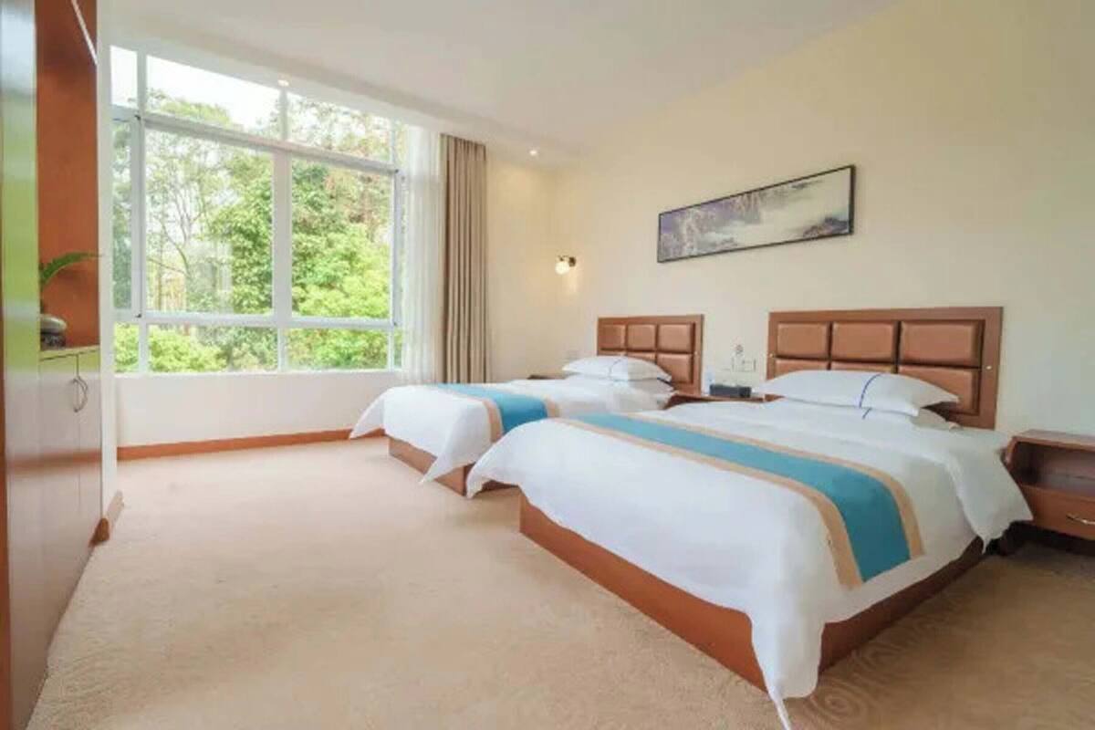 Une chambre d’hôtel avec deux lits, une grande fenêtre, un tableau au mur et une table de chevet.
