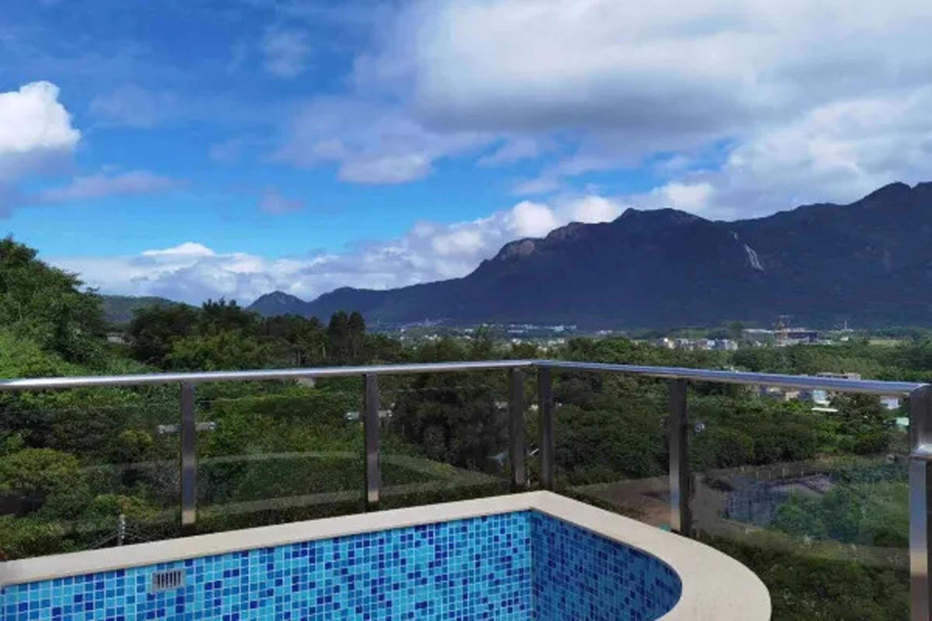 Une piscine dont le bord est revêtu de carreaux, entourée d’une rambarde en métal, avec en arrière-plan un paysage de montagnes et de verdure.