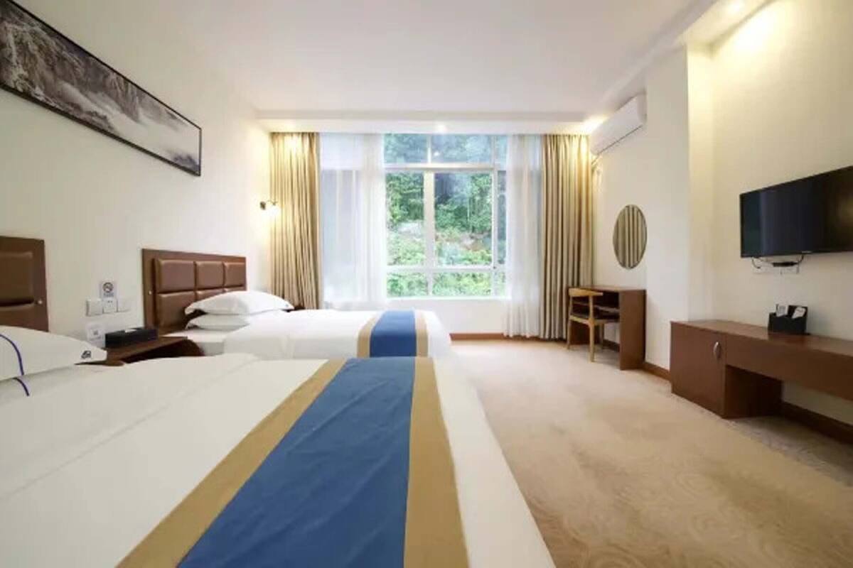 Une chambre d’hôtel avec deux lits, une télévision, un bureau et une fenêtre avec des rideaux.
