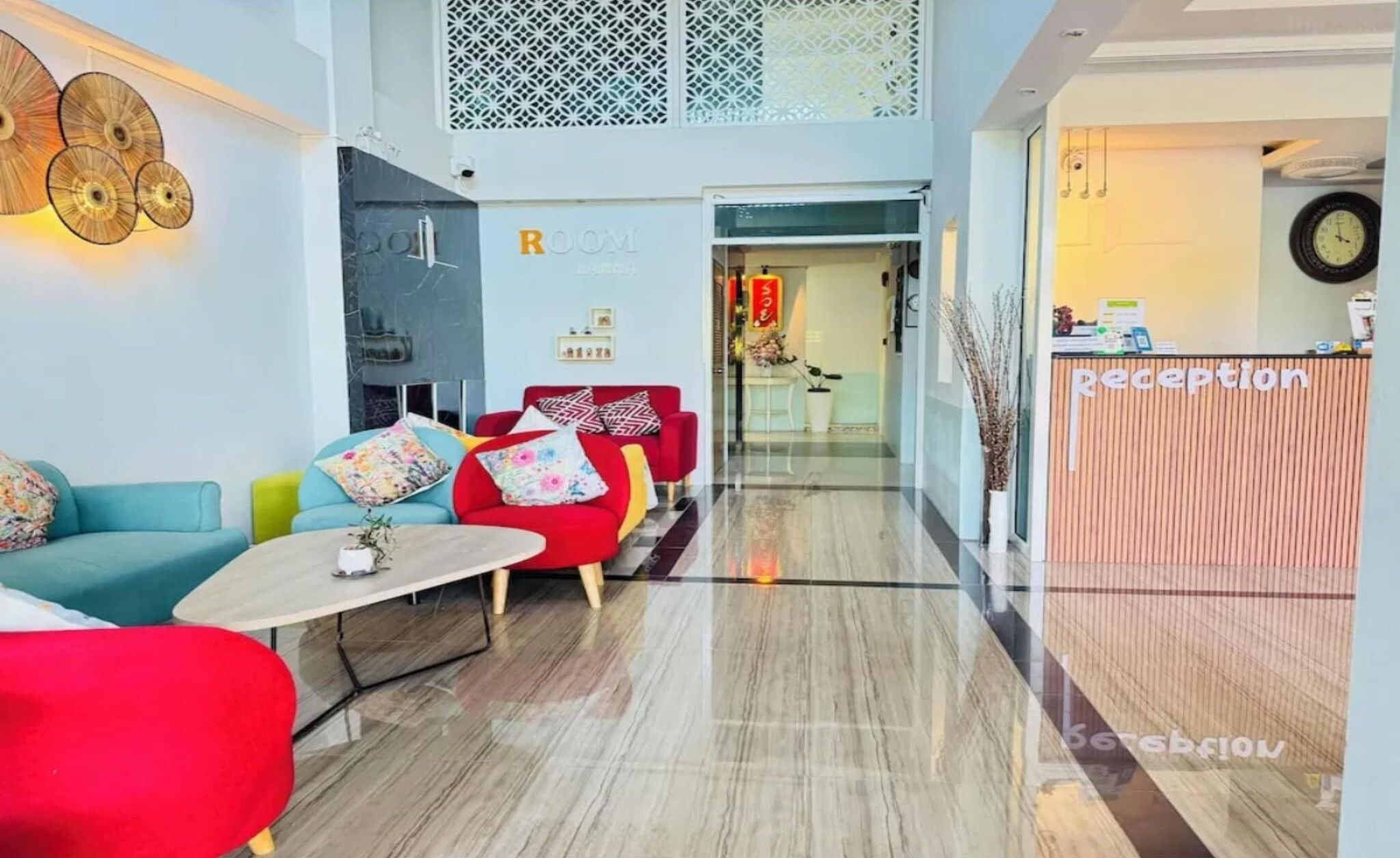 Et moderne receptionområde med en receptionsdisk, et siddeområde i røde og blå farver og udsigt ind til hotellets lobby.
