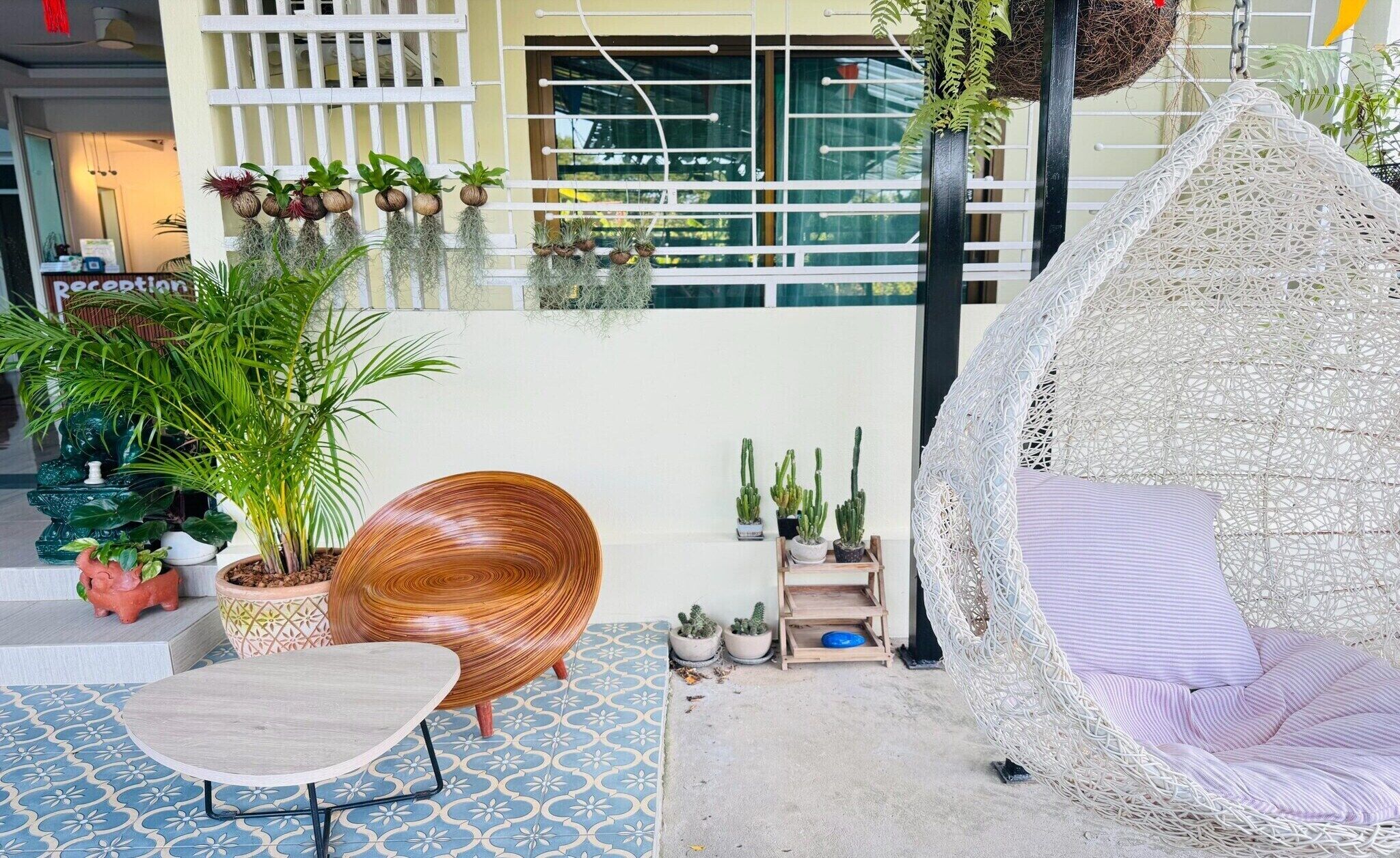 A cozy outdoor seating area with a woven hanging chair, a round wooden chair, and a variety of potted plants.