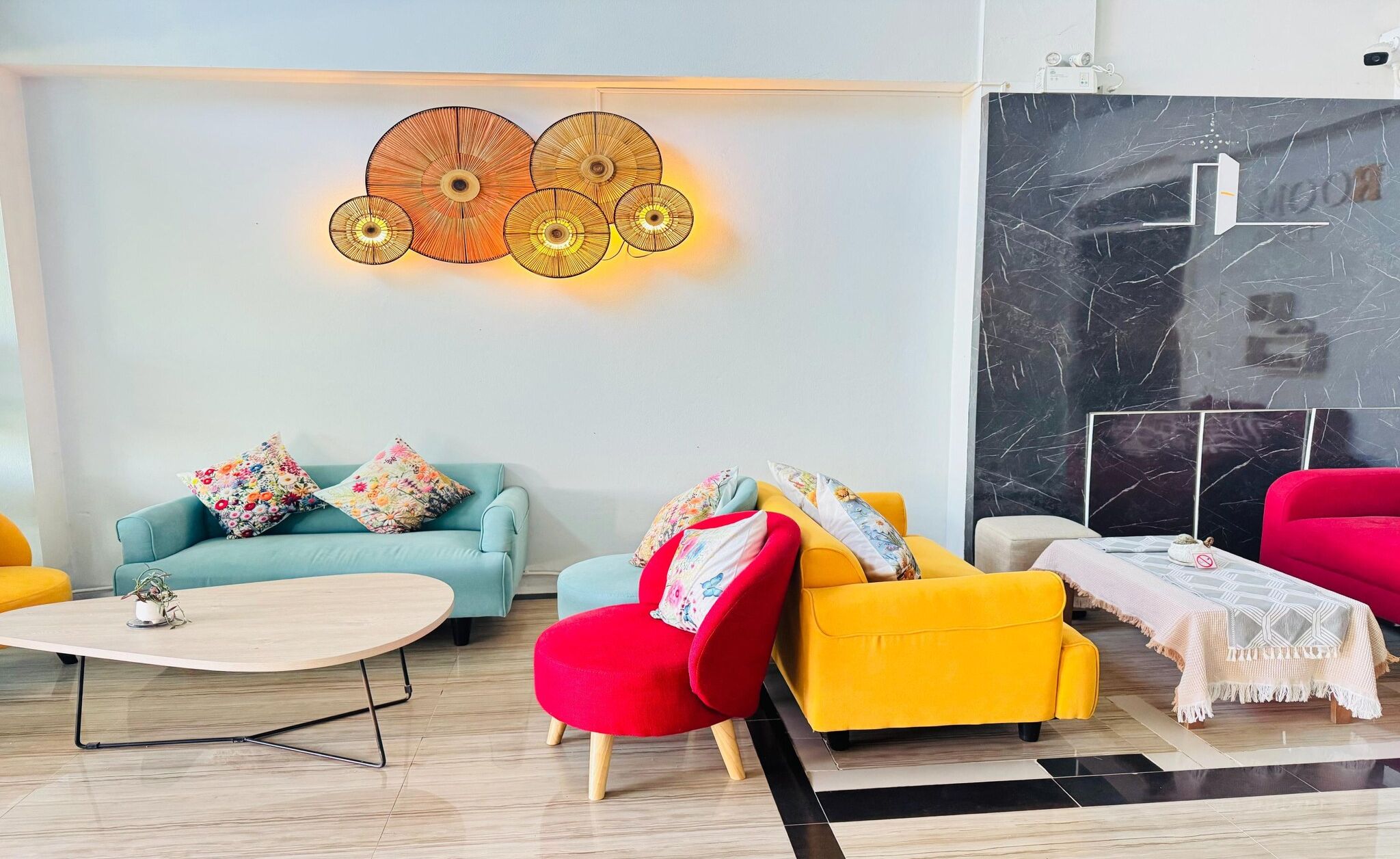 A modern living room with a light-colored sofa, a red armchair, and a yellow armchair. There is a coffee table in the center, and a decorative wall piece above the sofa.