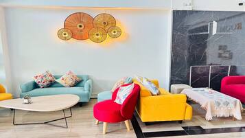 A modern living room with a light-colored sofa, a red armchair, and a yellow armchair. There is a coffee table in the center, and a decorative wall piece above the sofa.