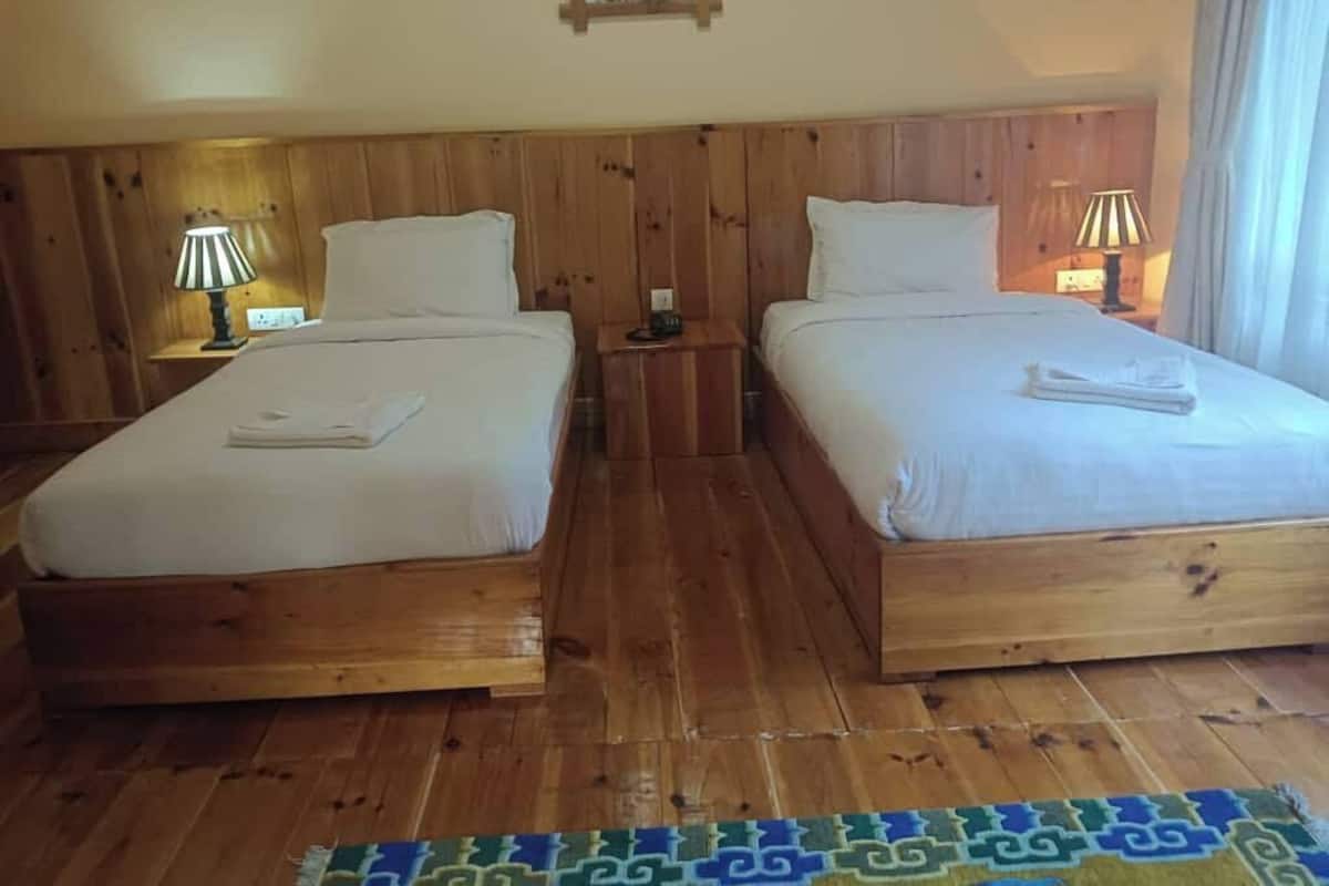 A room with two wooden beds, a small table with a lamp, and a framed picture on the wall.