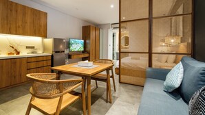 A modern kitchen with wooden cabinets, a dining table with chairs, a sofa, and a TV. - Forseti Athena by ARM One Hundred (Denpasar)