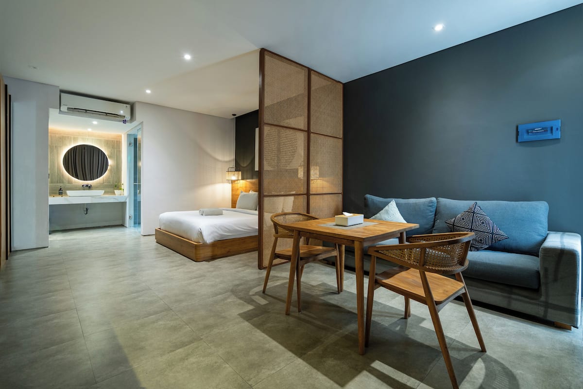 Une chambre d’hôtel moderne comprenant un lit, un coin repas avec une table et des chaises, un canapé et une grande fenêtre.