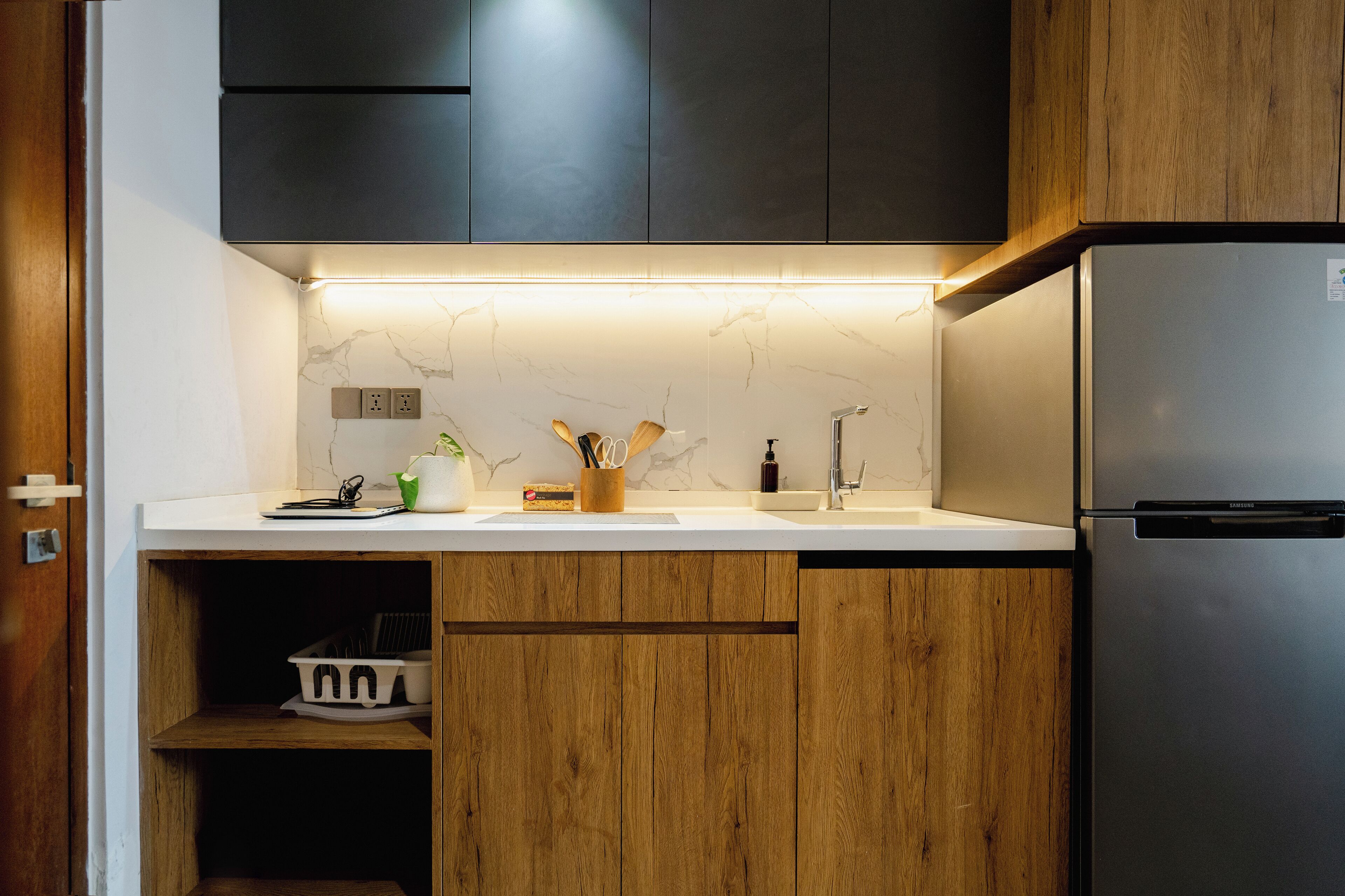 A modern kitchen with wooden cabinets, a stainless steel refrigerator, and a marble backsplash.