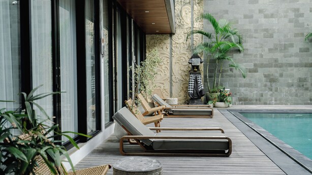 A poolside area with lounge chairs, a stone table, and potted plants. - Forseti Athena by ARM One Hundred (Denpasar)