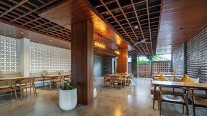 A spacious indoor area with wooden tables and chairs, a large white planter, and a ceiling with a grid pattern. - Forseti Athena by ARM One Hundred (Denpasar)
