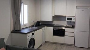A compact kitchen with white cabinets, a built-in oven, a microwave, and a washing machine. - Apartamento 2B in Malaga (Málaga)