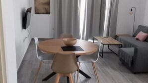 A modern living room with a round wooden dining table, grey upholstered chairs, a grey sofa, and a small wooden coffee table. - Apartamento 2B in Malaga (Málaga)