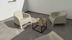 A modern outdoor seating area with two white plastic chairs, a small table with food and drinks, and a window. - Apartamento 1B in Malaga (Málaga)