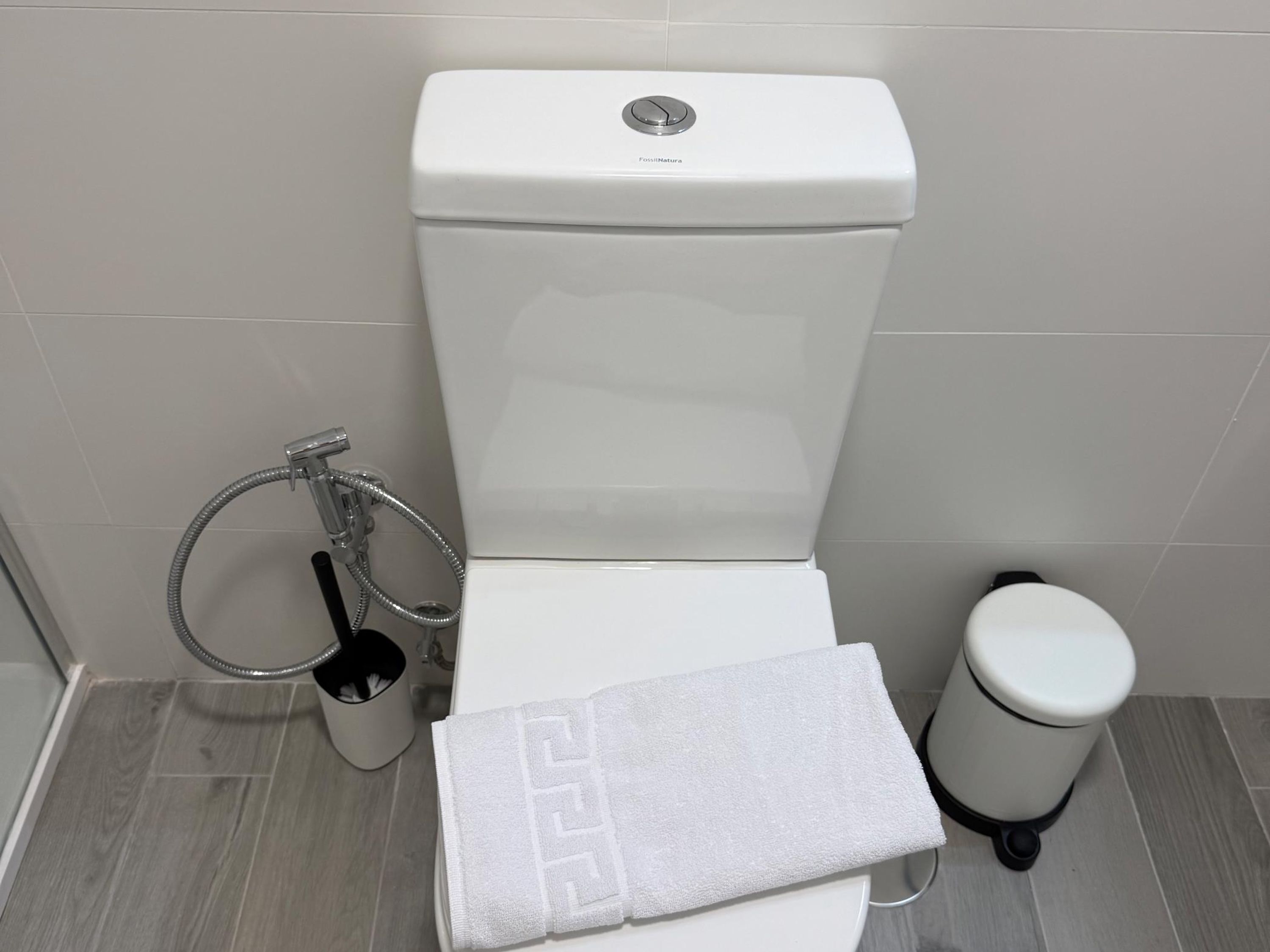 Des toilettes blanches dotées d’une molette de commande, un abattant-bidet argenté et une poubelle blanche.