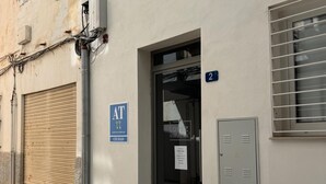 A building with a closed shutter, a blue sign indicating a public toilet, and a door with a number sign. - Apartamento 1A in Malaga (Málaga)