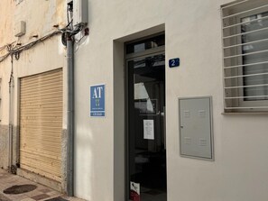 A building with a closed shutter, a blue sign indicating a public toilet, and a door with a number sign. - Apartamento 1A in Malaga (Málaga)