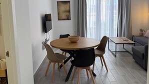 A modern living room with a round wooden dining table, two black chairs, a grey sofa, and a small side table. - Apartamento 1A in Malaga (Málaga)