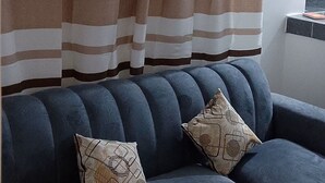 Un canapé bleu foncé agrémenté de deux coussins à motifs, un rideau à rayures et une petite table sur laquelle repose un livre.