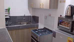 Une cuisine de taille réduite équipée d’une cuisinière à gaz, d’un four à micro-ondes, d’un réfrigérateur et de meubles de rangement en bois.