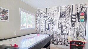 Ett rum med ett biljardbord, ett fönster med persienner och en vägg prydd med en väggmålning som föreställer en stadsbild.