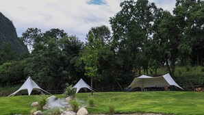A campsite with tents, a pond, and a grassy area with trees in the background. - YINGMAN HOTEL (Guilin)