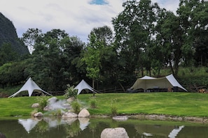 A campsite with tents, a pond, and a grassy area with trees in the background. - YINGMAN HOTEL (Guilin)