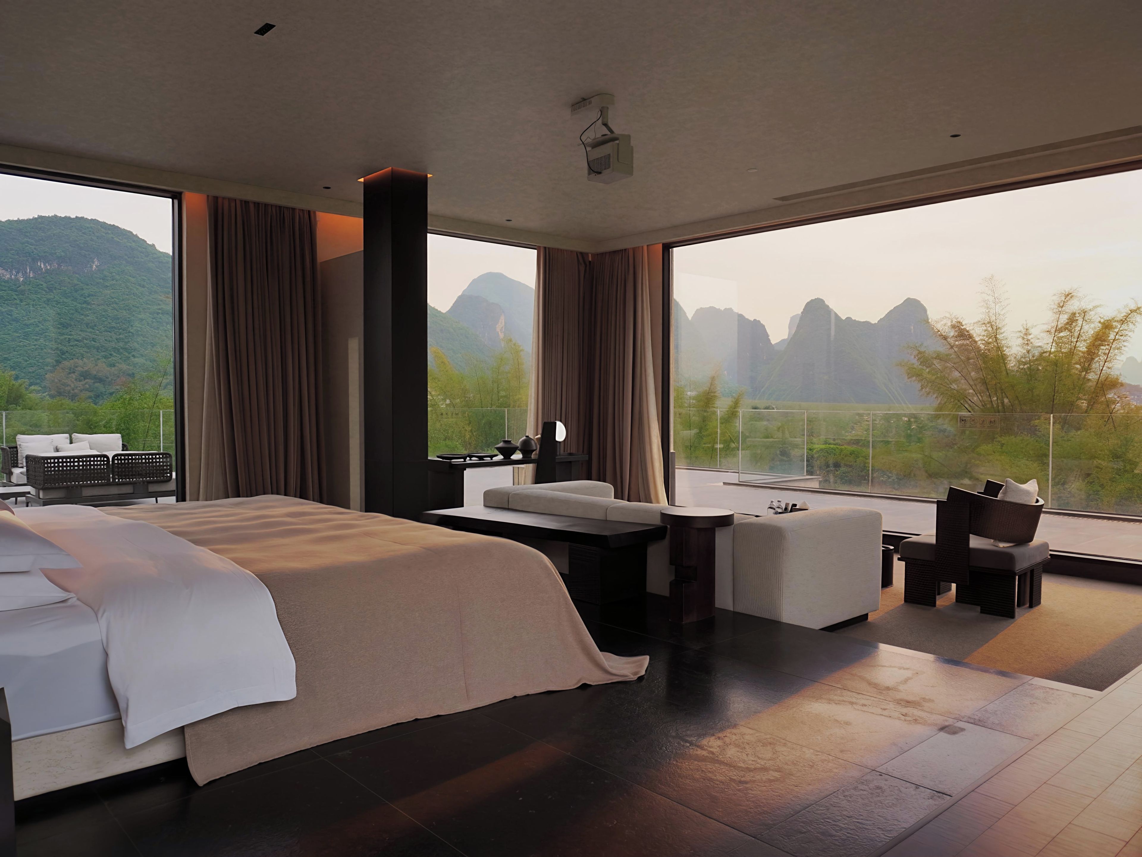 A modern hotel room with a large bed, a seating area, and a balcony with a mountain view.