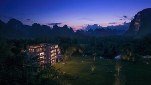 A modern hotel with multiple floors and a well-lit exterior, surrounded by a lush green landscape and mountains in the background. - YINGMAN HOTEL (Guilin)