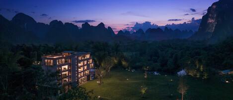 Un hotel moderno con diversi piani ed esterno luminoso, immerso in un paesaggio verdeggiante con montagne sullo sfondo.