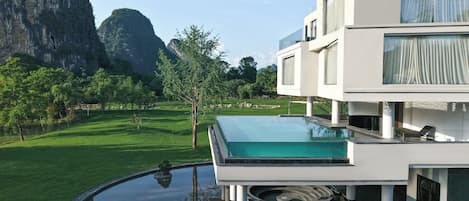 Una casa moderna con piscina infinita de cristal, césped bien cuidado y vistas a la montaña.