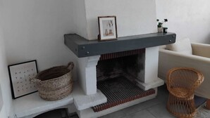 Una chimenea con repisa, un cuadro enmarcado, una cesta de mimbre y un sillón de mimbre.
