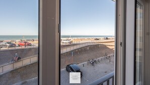 A view from a window overlooking a beach with cars parked along the roadside and a sign indicating 'Floor 1, Season 1'. - The Corner Floor, front row sea view and parking (Oostende)