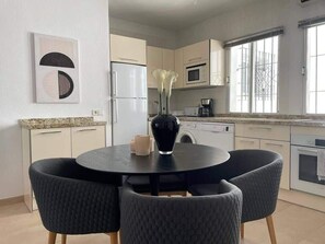 Een moderne keuken met een ronde eettafel, stoelen, een koelkast, magnetron, oven en een groot raam.