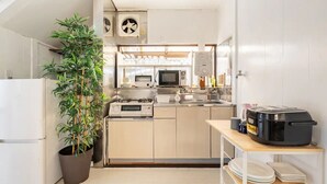 Une cuisine compacte équipée d’un four à micro-ondes, d’une cuisinière et d’un évier. On y trouve une plante en pot et une petite table sur laquelle est posé un cuiseur à riz.